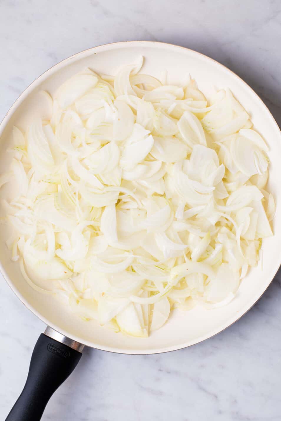 Sliced raw onions in a white skillet.