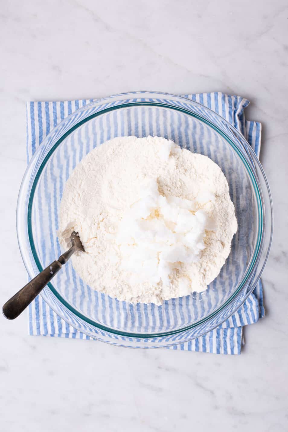 Flour and coconut oil in a glass bowl with a fork.