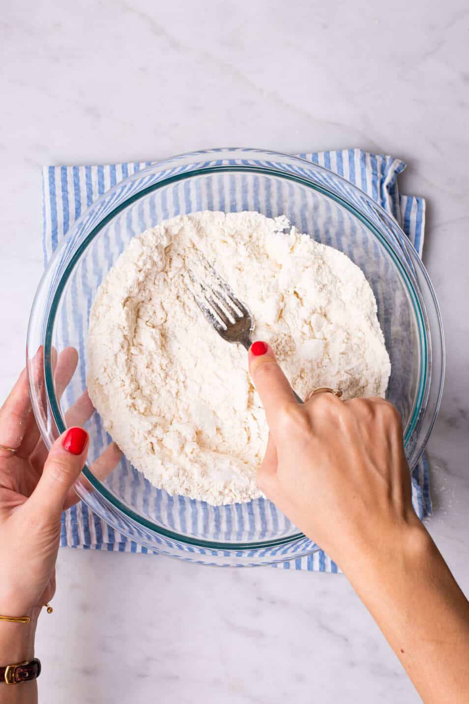 Woman's hand mashing coconut oil into flour with a fork.