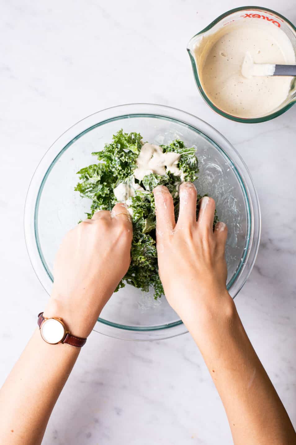 Woman's hands massaging kale with creamy cashew dressing.