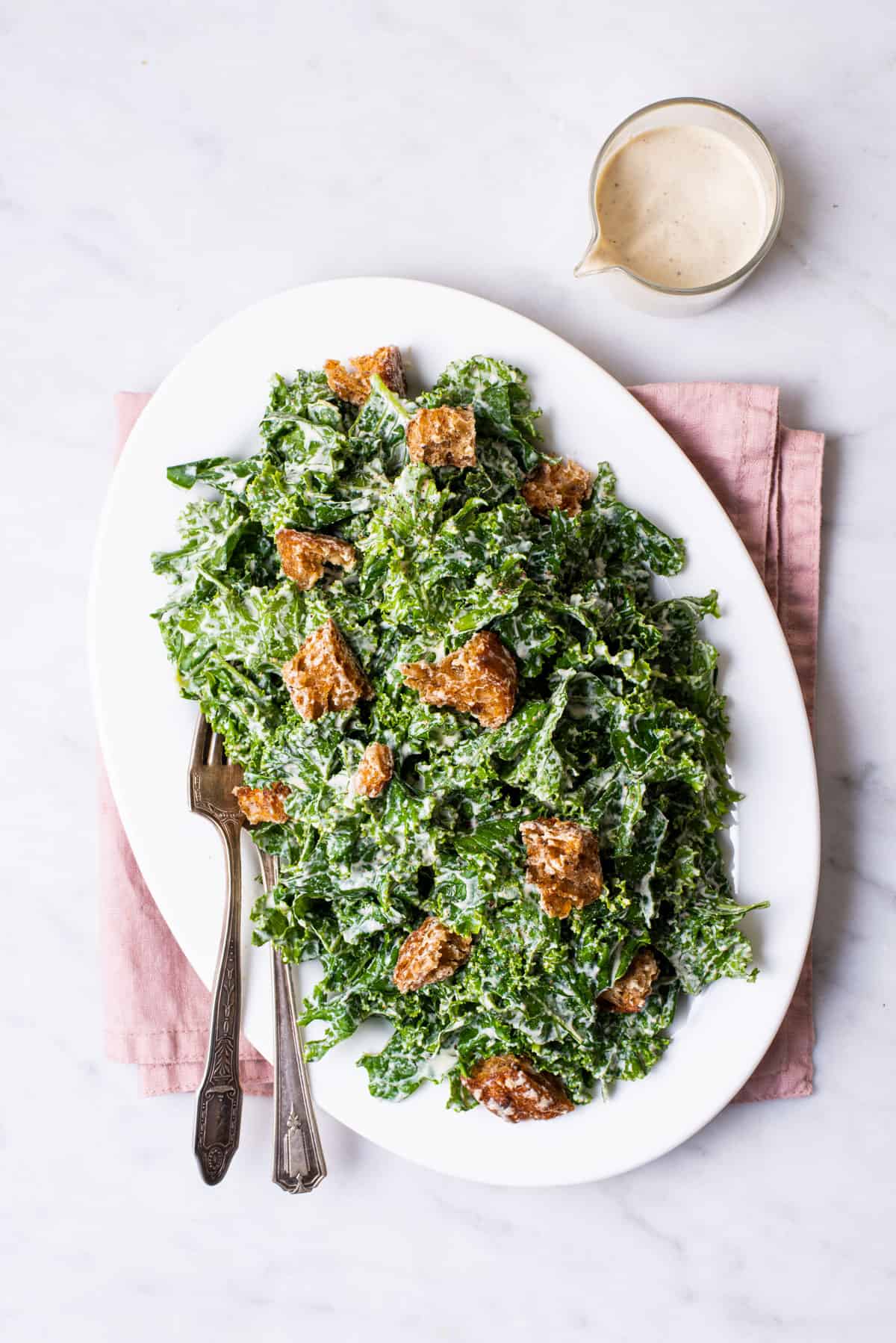 Massaged cashew kale caesar salad on an oval platter on a marble table.