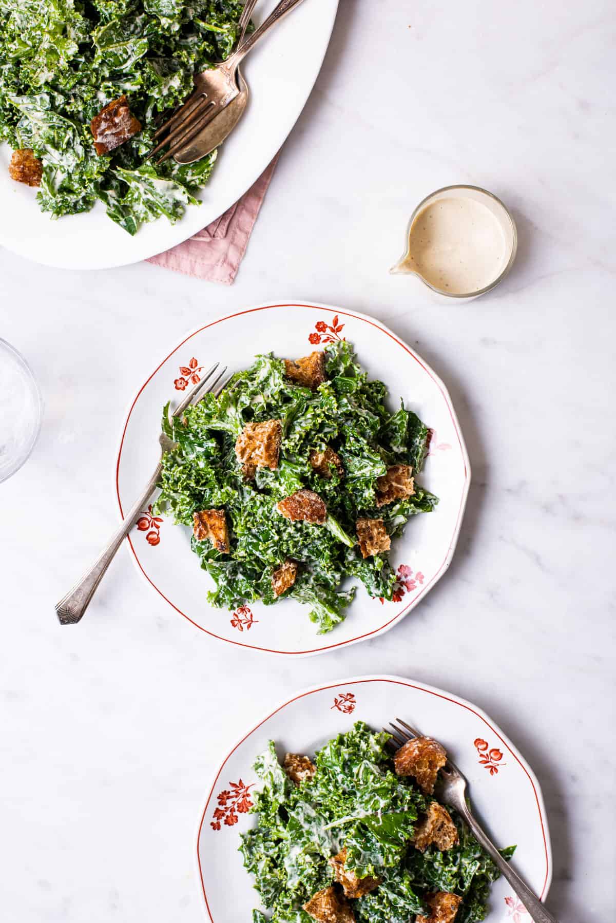 Vegan kale caesar salad with homemade croutons on white plates.