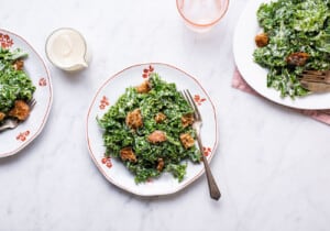 Massaged cashew kale caesar salad with rustic breadcrumbs on vintage plates on a marble table.