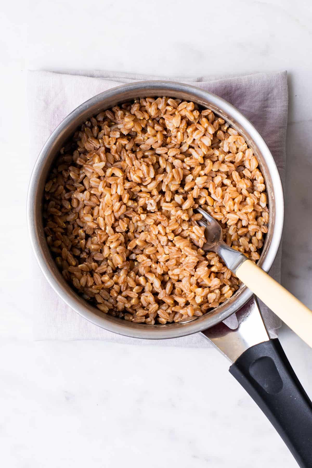 Cooked farro in a small pot with a fork.