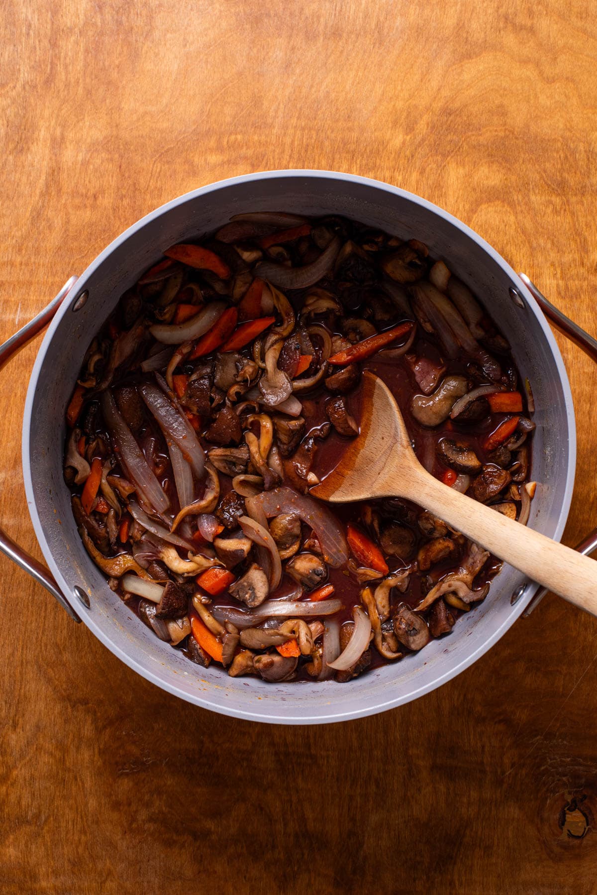 Pouring red wine into a pot with sauteed carrots and onions.