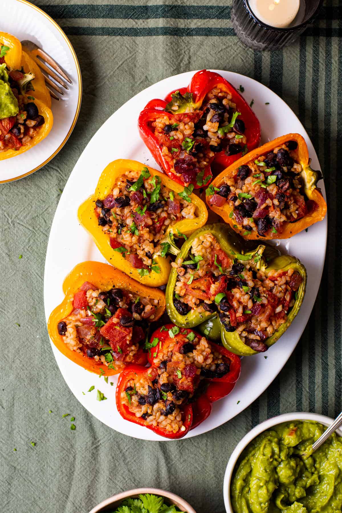 Vegan Mexican stuffed peppers on an oval platter on a green tablecloth.