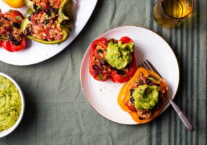 Vegan Mexican stuffed peppers with guacamole on a plate on a green tablecloth.