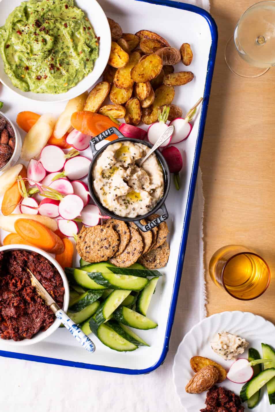 A festive vegan snack board with a trio of dips, colorful crudités, and roasted baby potatoes.