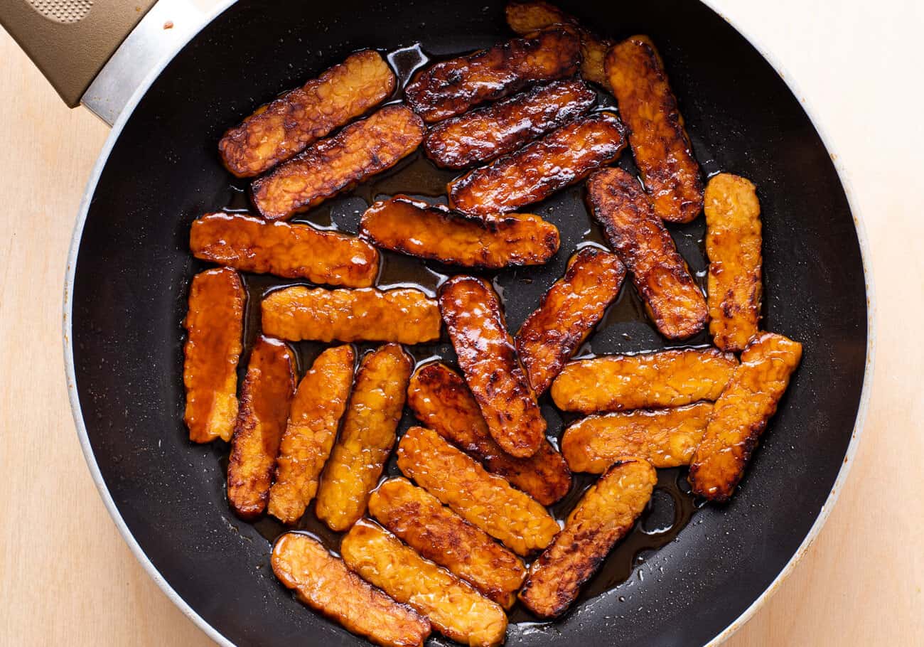 Glazed tempeh slices in a skillet.