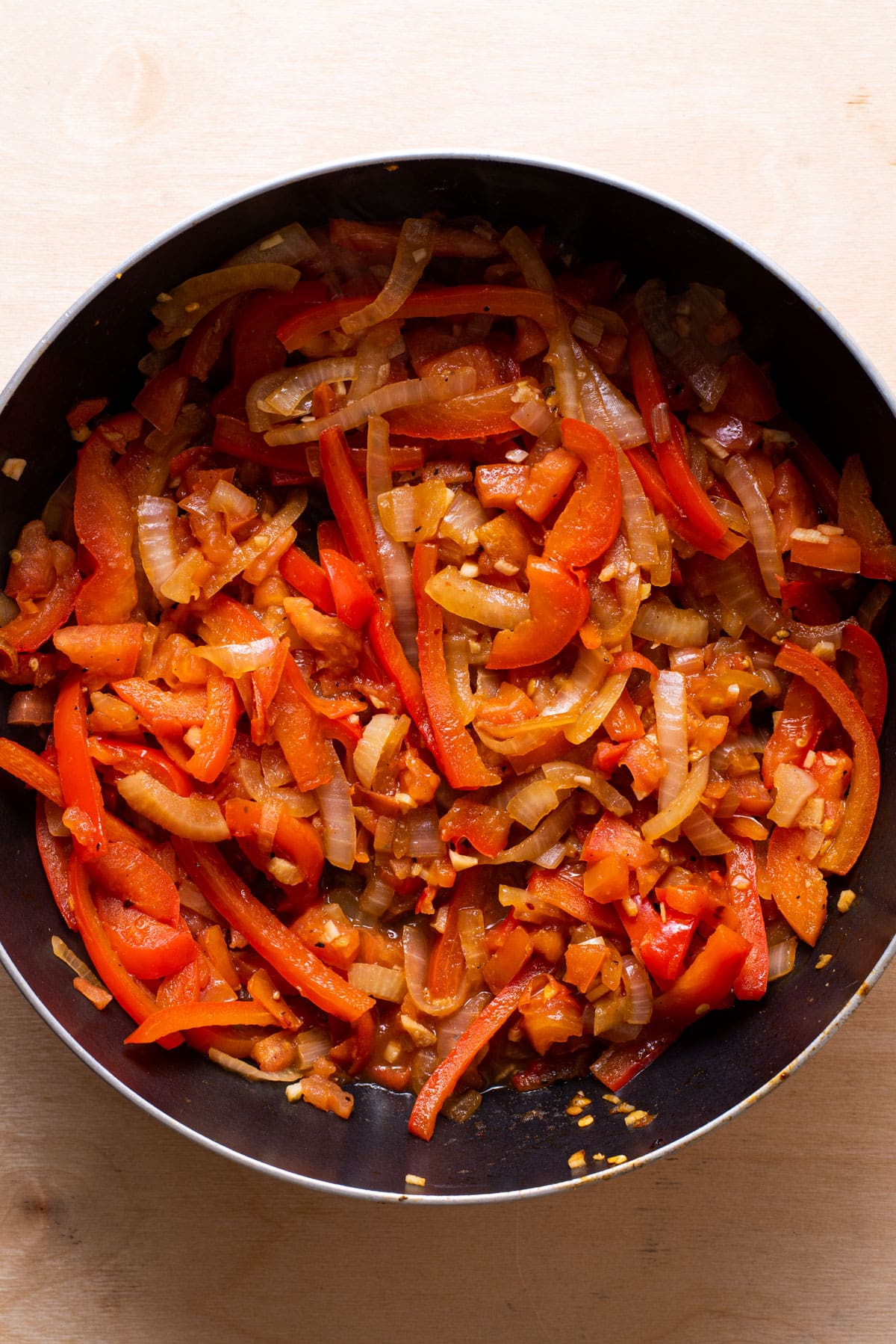 Peppers, onions, and tomatoes sauteed in a saucepan.