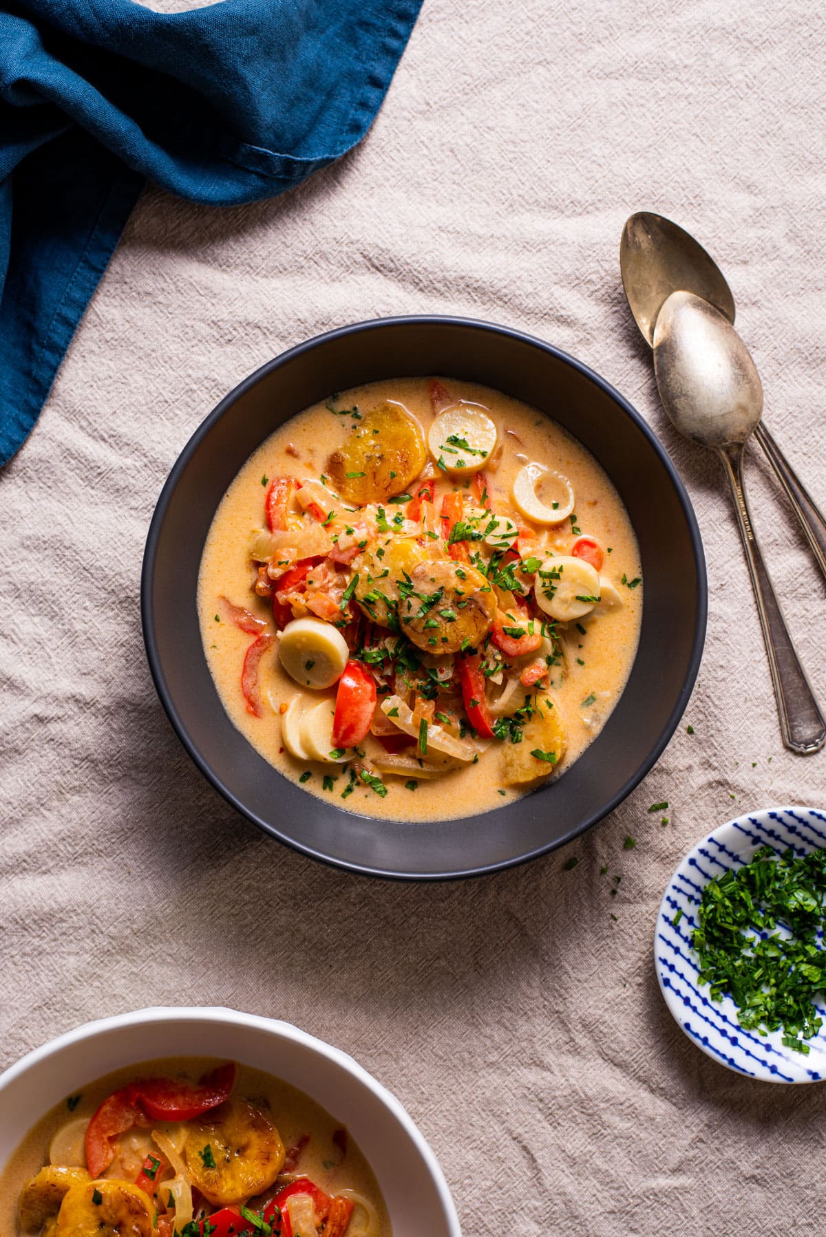 Vegetarian moqueca with plantains and hearts of palm in a black bowl next to chopped parsley.