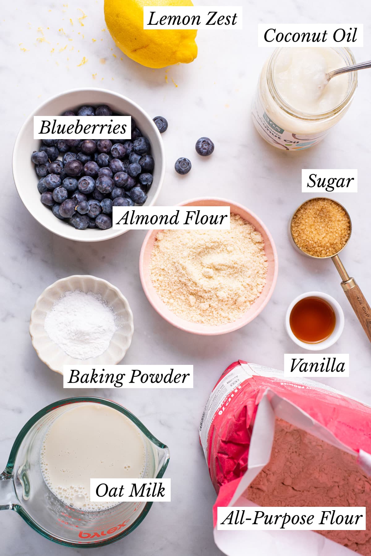 Ingredients gathered to make vegan blueberry lemon muffins on a marble counter.