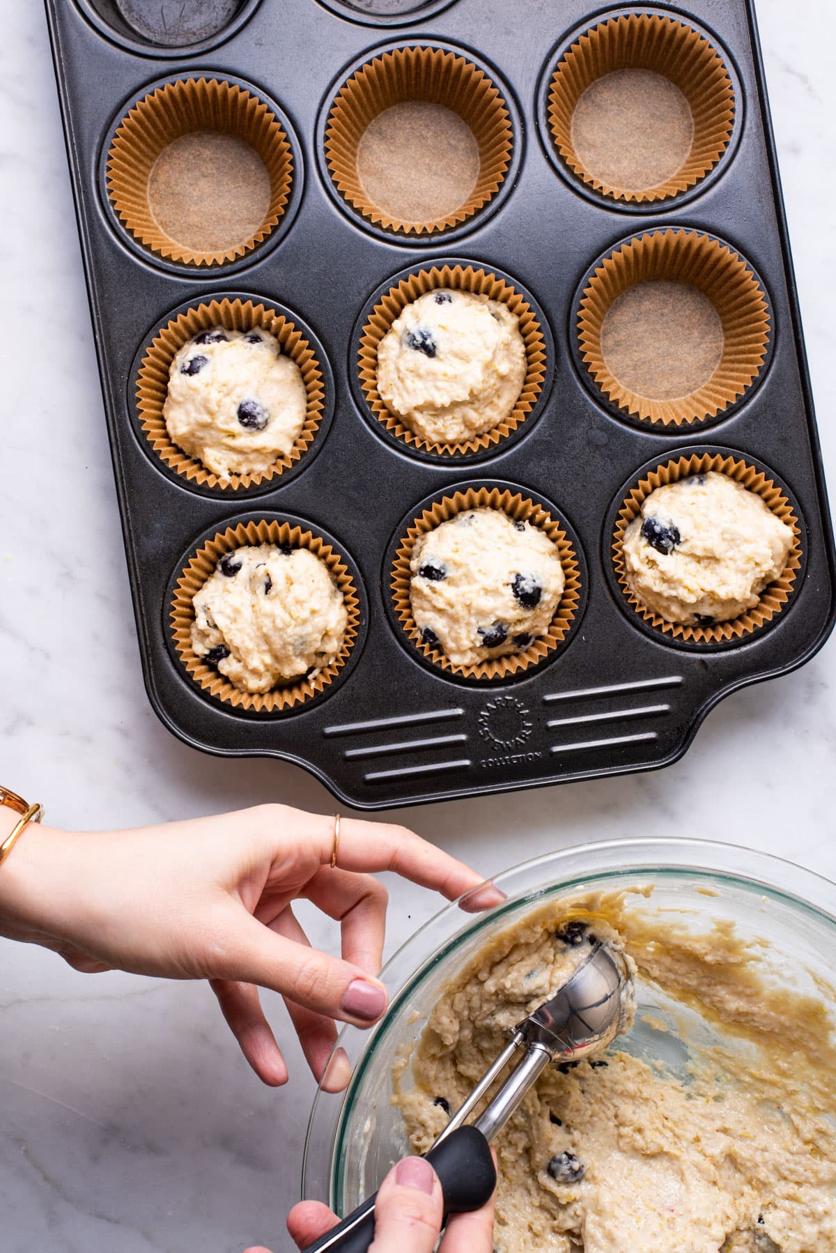 Woman's hand scooping batter into muffin tin with ice cream scoop.