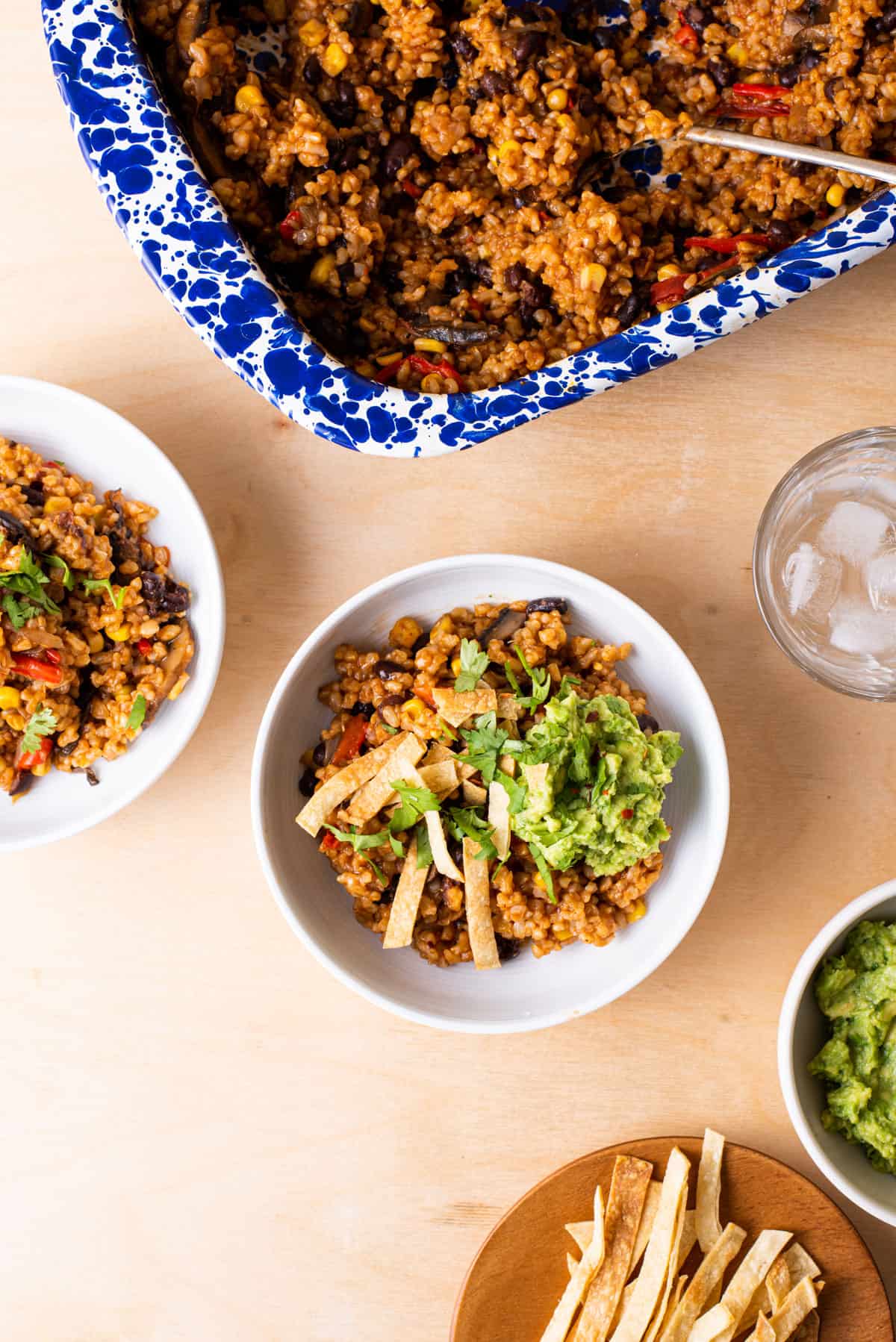 Mexican vegan rice casserole in white bowls with tortilla strips and guacamole.