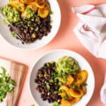 Black beans and plantains in white bowls with guacamole, next to cilantro and limes.