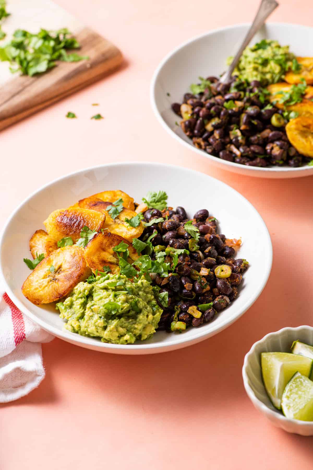 Black bean bowls with plantains and guacamole on a pink table.