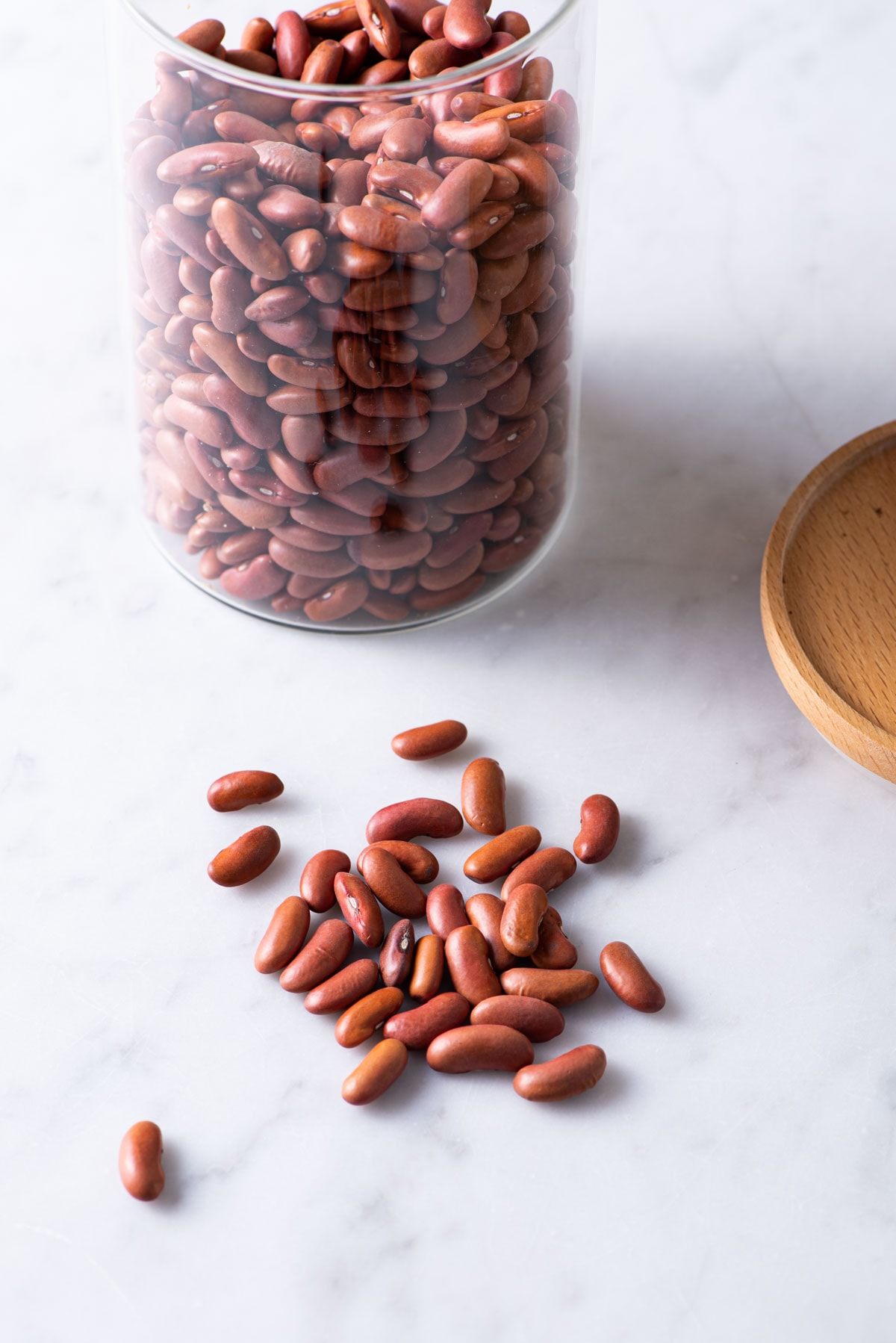 Kidney beans on a marble table next to a glass jar.