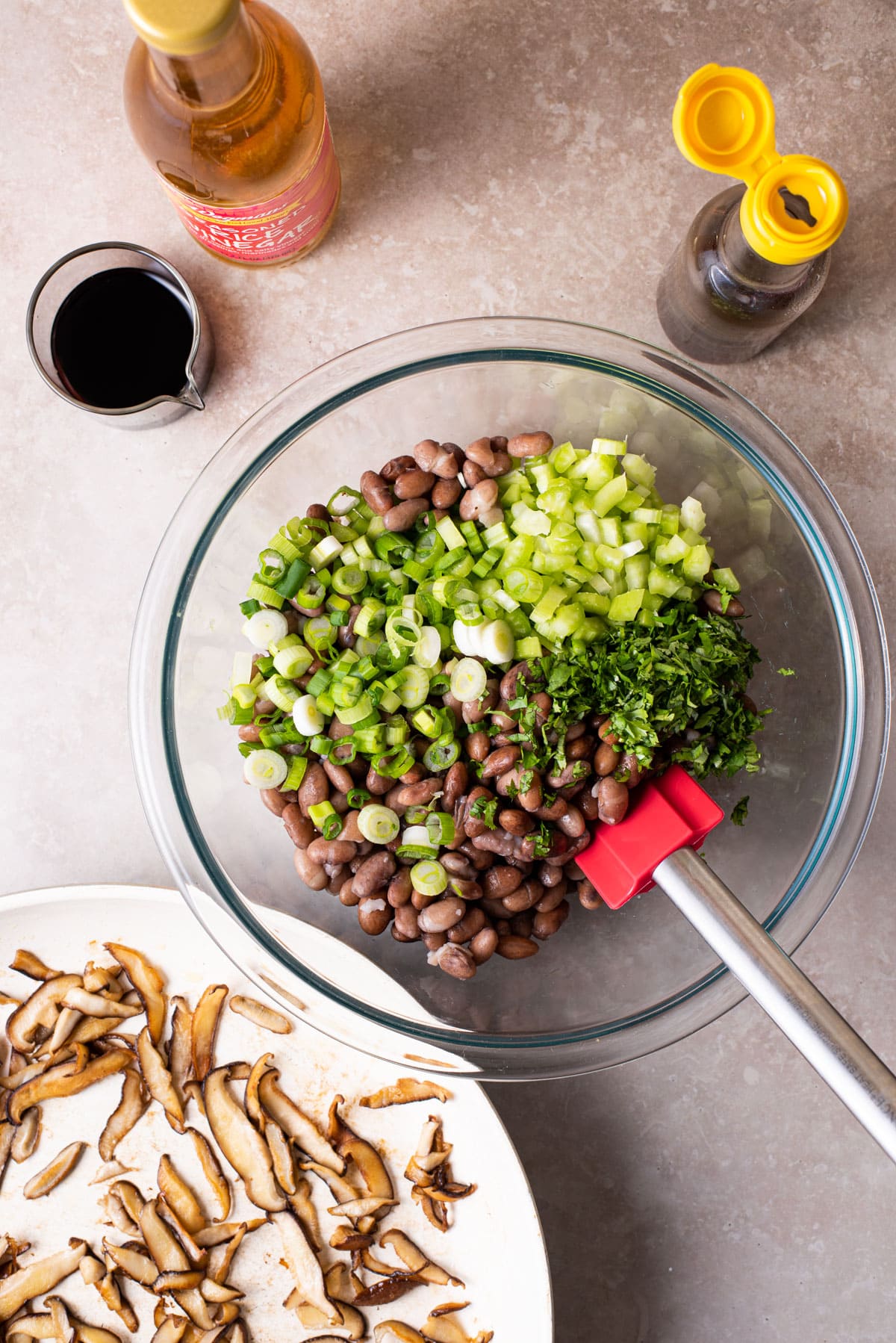 Beans and chopped herbs in a glass bowl, next to sauteed mushrooms.