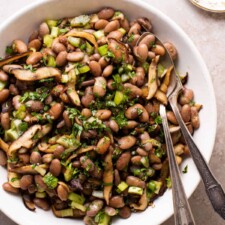 Vegan pinto bean salad with shiitake mushrooms and herbs in a white bowl.
