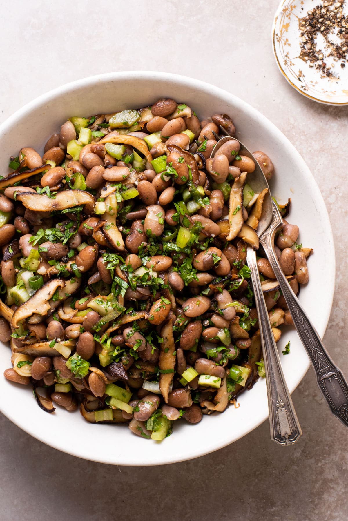Vegan pinto bean salad with shiitake mushrooms and herbs in a white bowl.