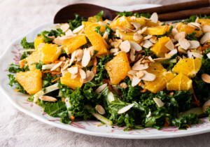 Kale fennel salad with oranges and sliced almonds on an oval platter with wooden spoons.