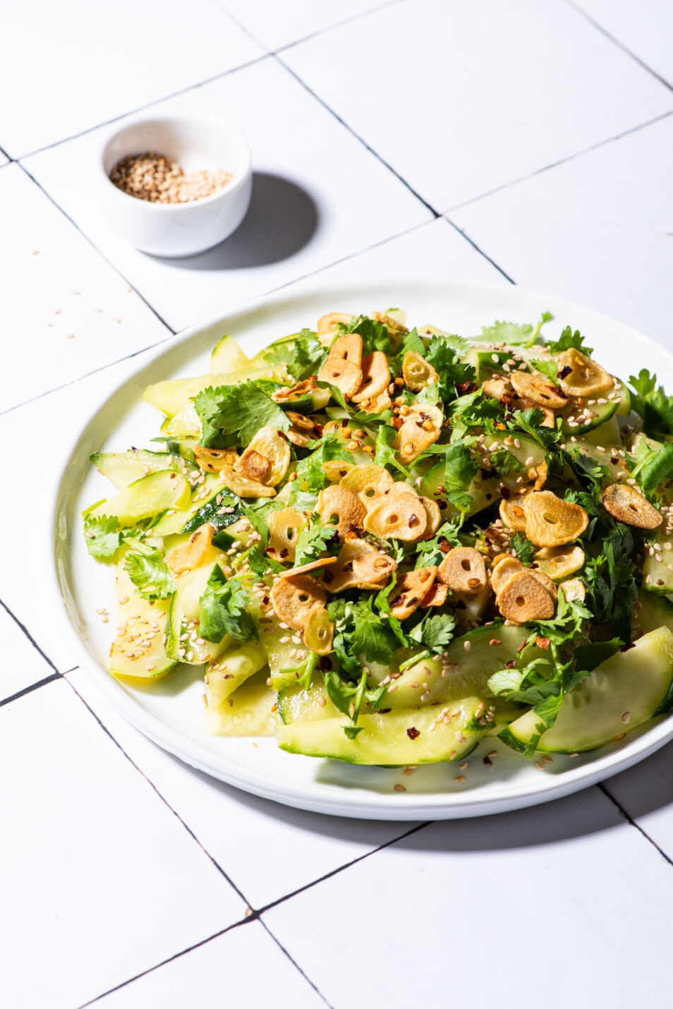 Healthy summer salad made of cucumbers, garlic chips, and cilantro, on a white plate.
