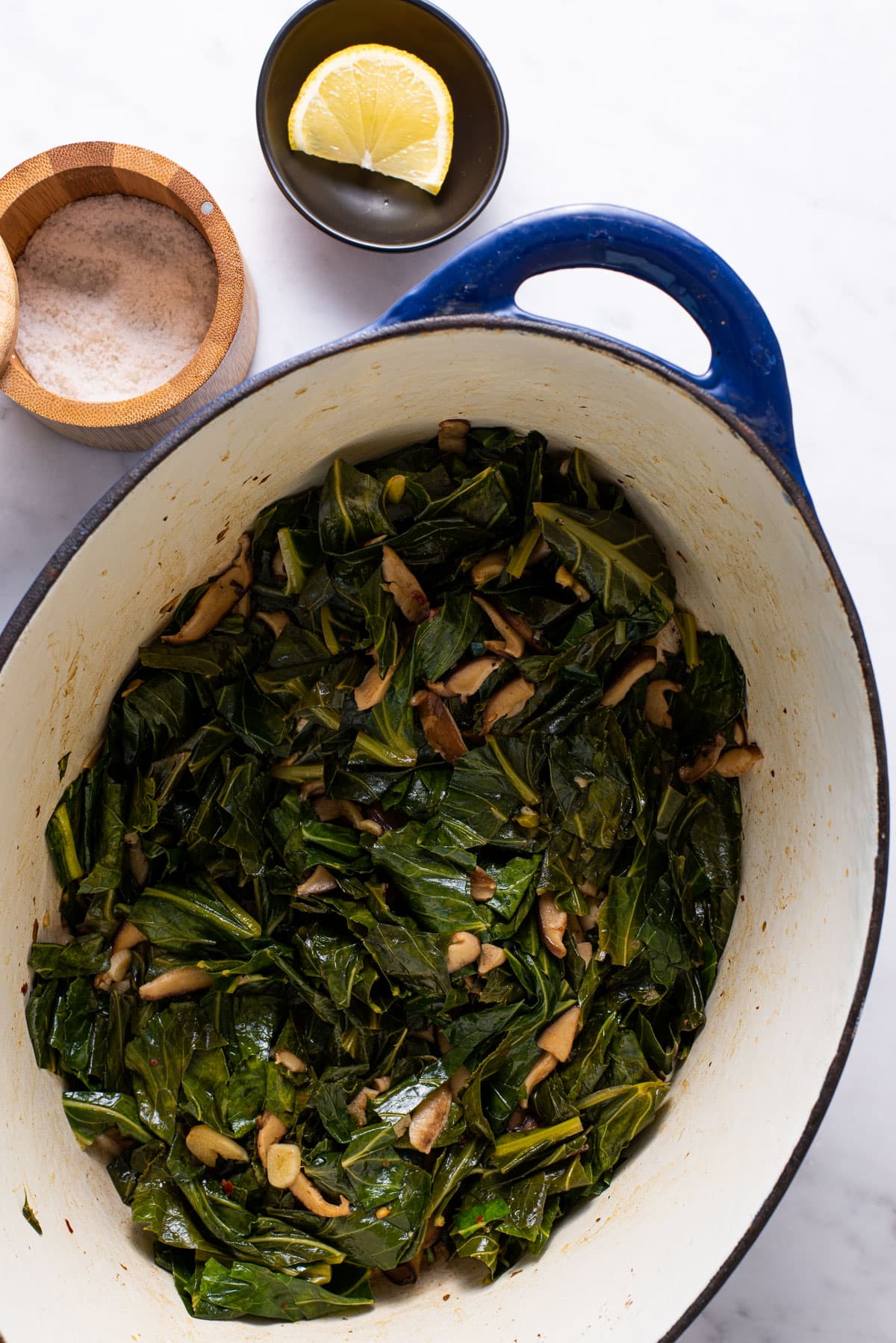 Braised collard greens in a Dutch oven next to lemon and salt.