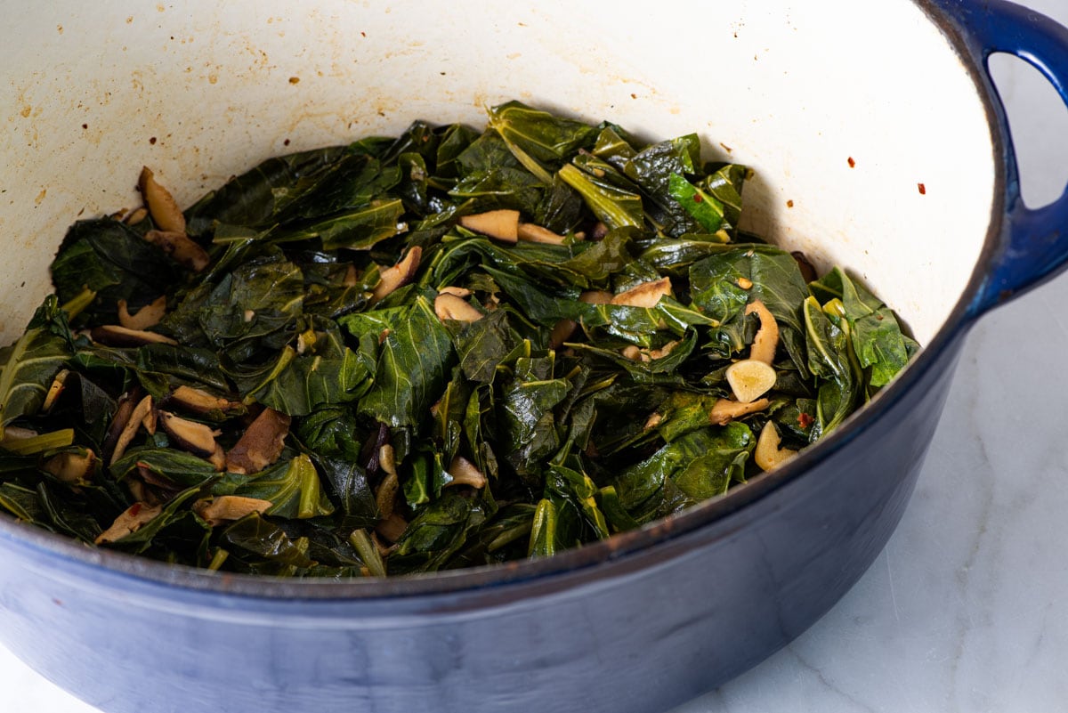 Braised collard greens with mushrooms in a Dutch oven.