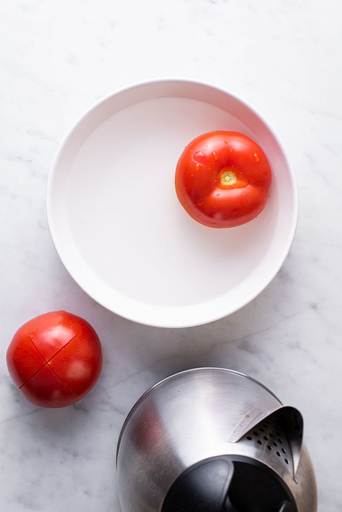 Vine tomatoes in a bowl of water next to a kettle.