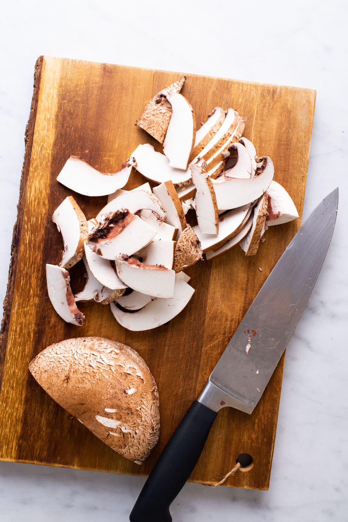Sliced portobello mushrooms on wooden cutting board.