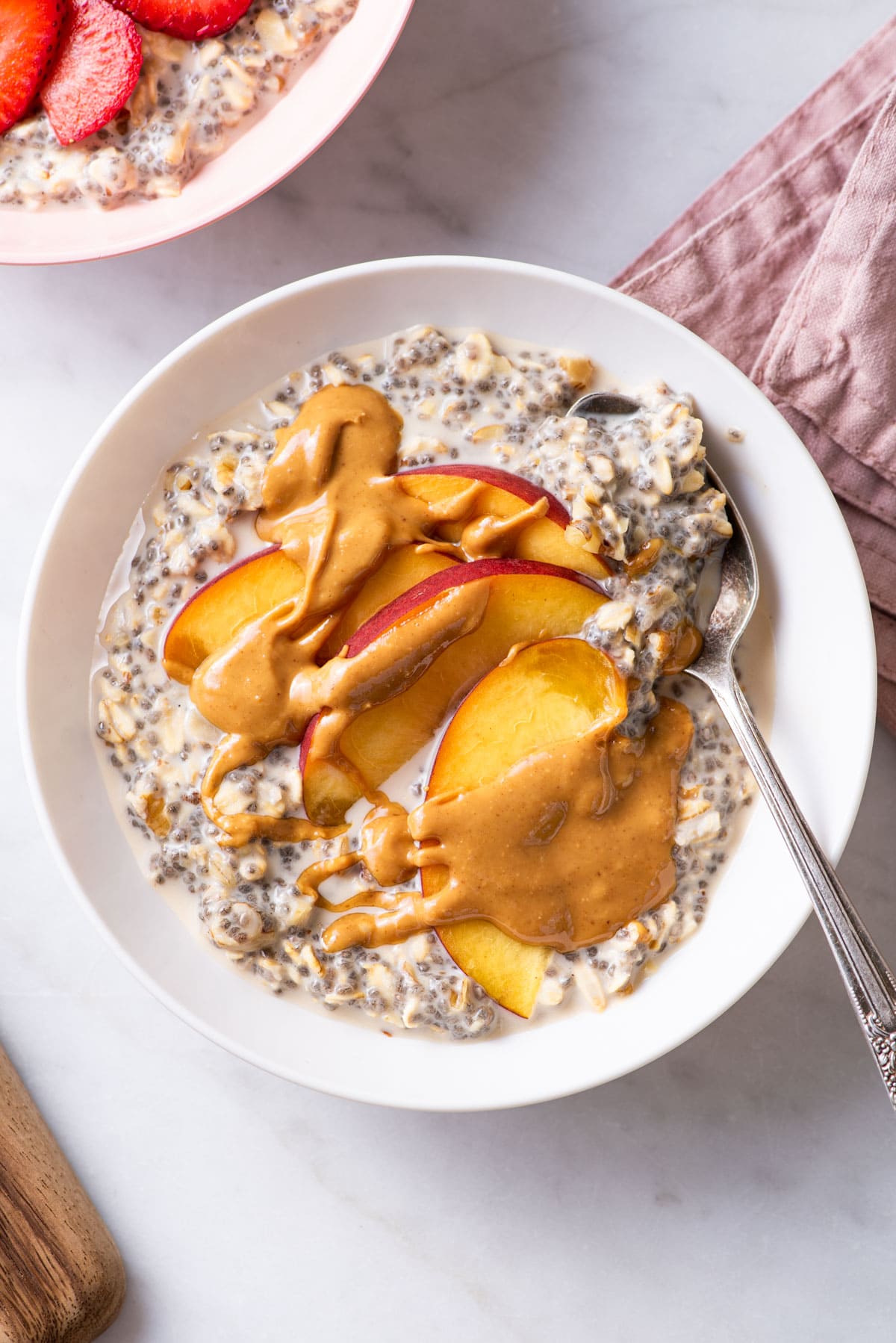 Overnight oats with chia seeds in a white bowl with peach slices and peanut butter.