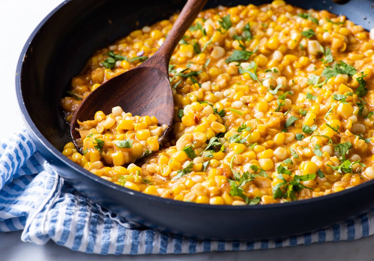 Vegan creamed corn in a skillet with a wooden spoon.