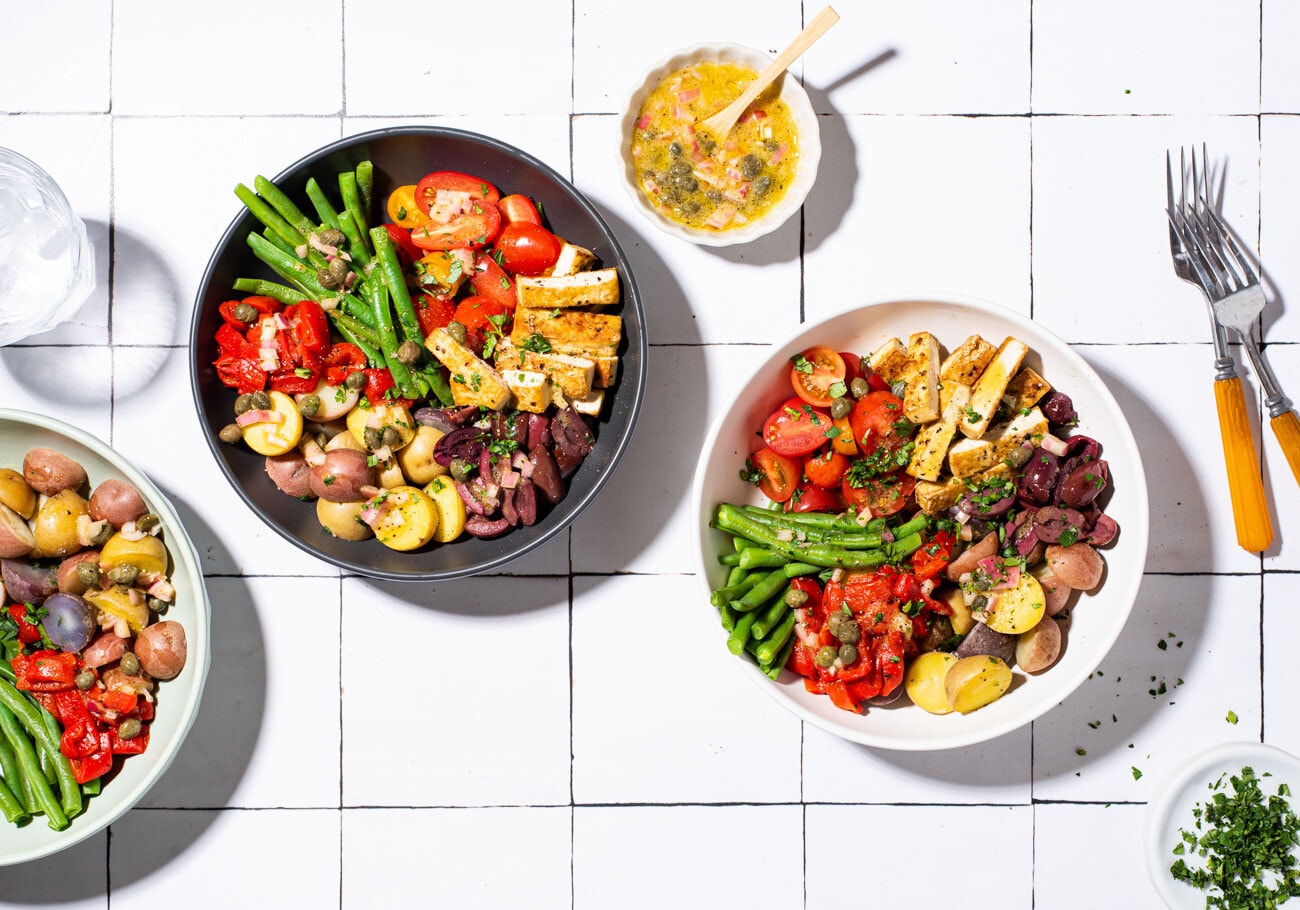 Vegan nicoise salad with tofu, in various bowls on a tiled table.