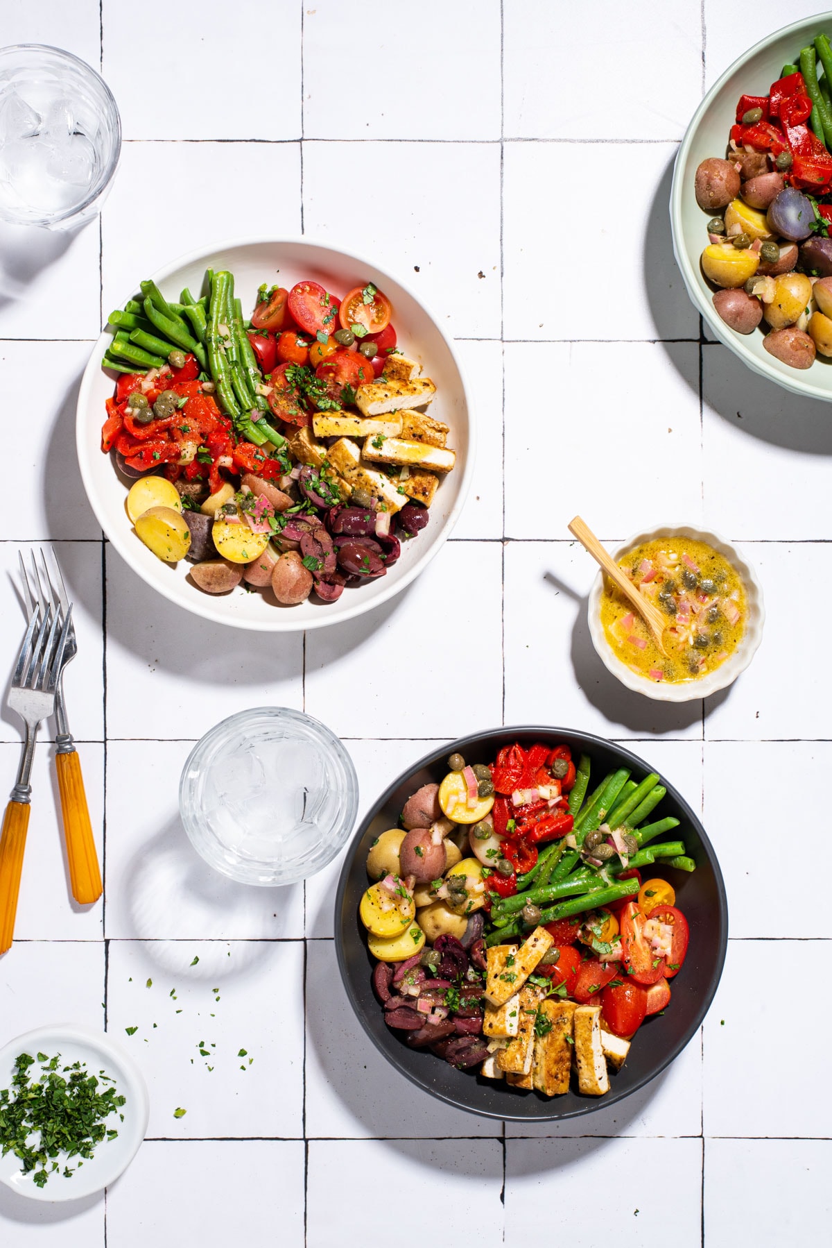 Vegan nicoise salad with tofu, in various bowls on a tiled table.