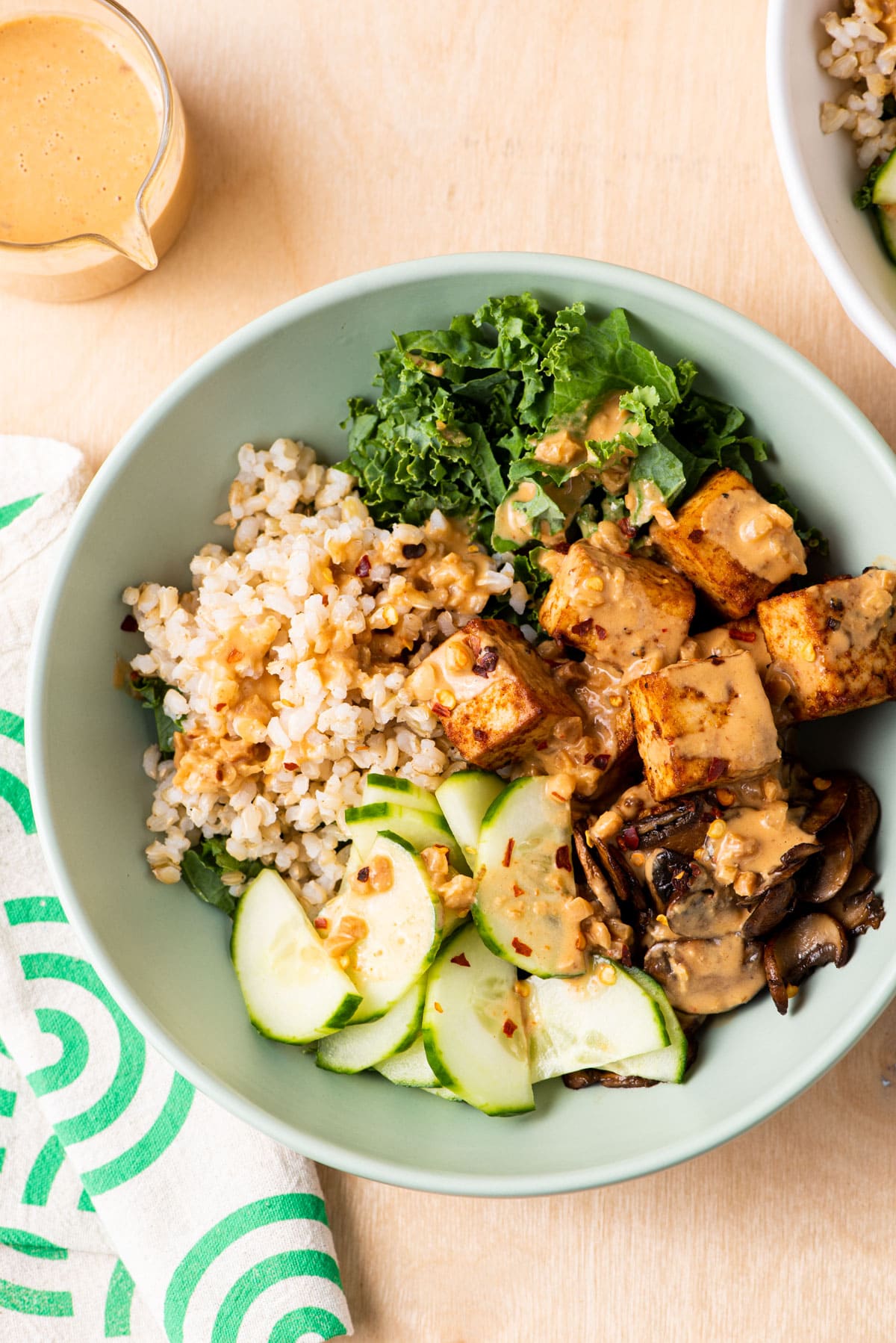 Tofu rice bowl with mushrooms, kale, cucumbers, and peanut sauce.