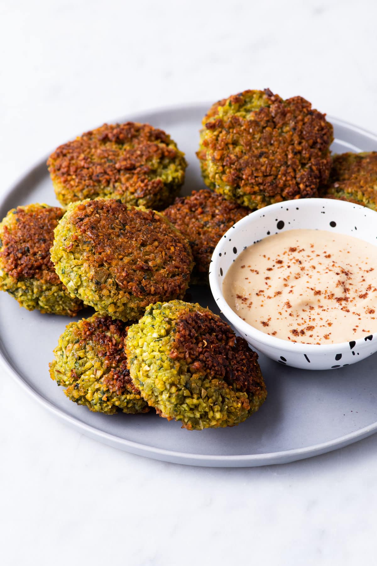 Baked falafel patties on a gray plate next to tahini sauce.