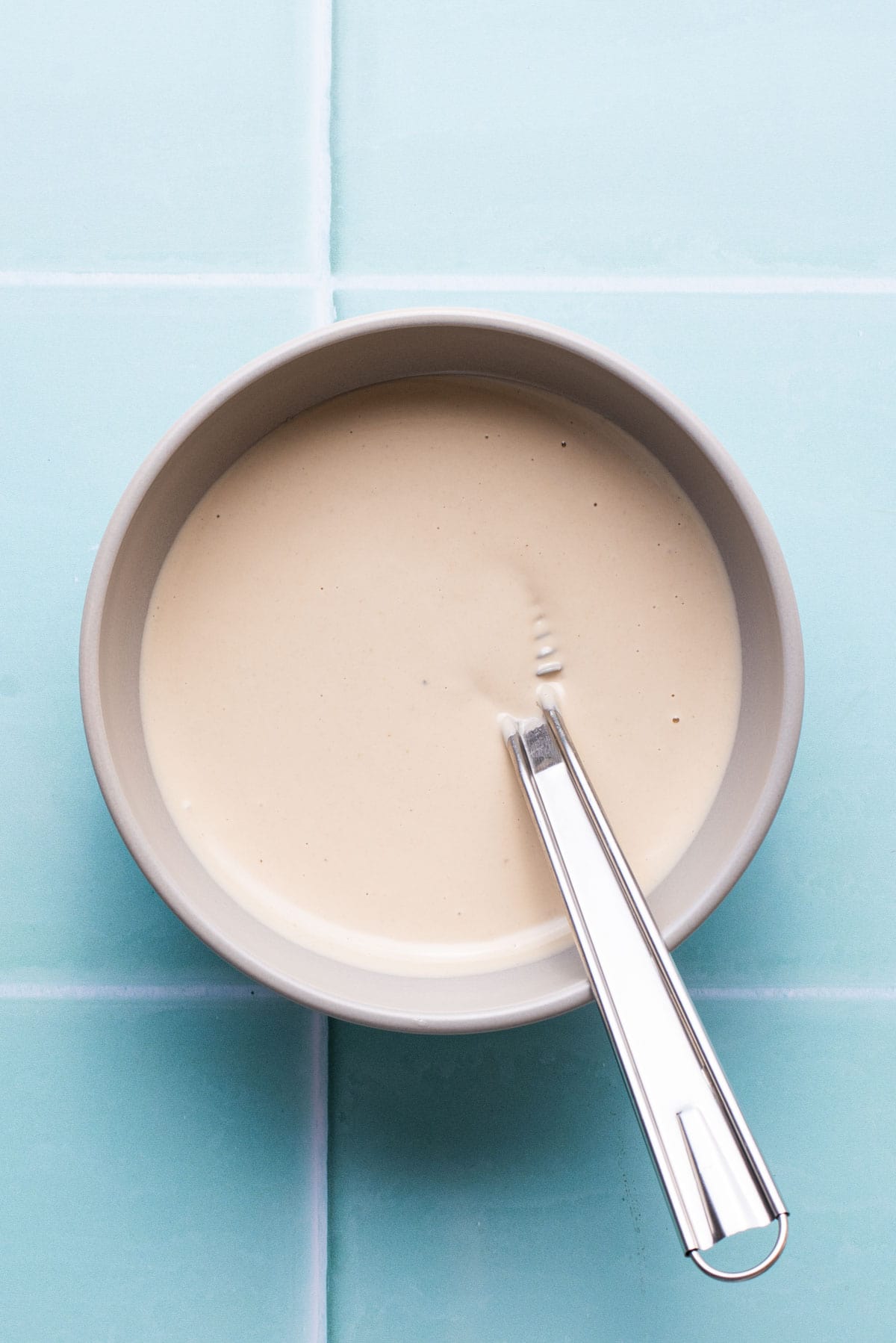 Tahini sauce in a bowl with a whisk.
