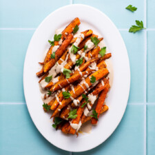 Spiced roasted carrots drizzled with tahini sauce on an oval platter.