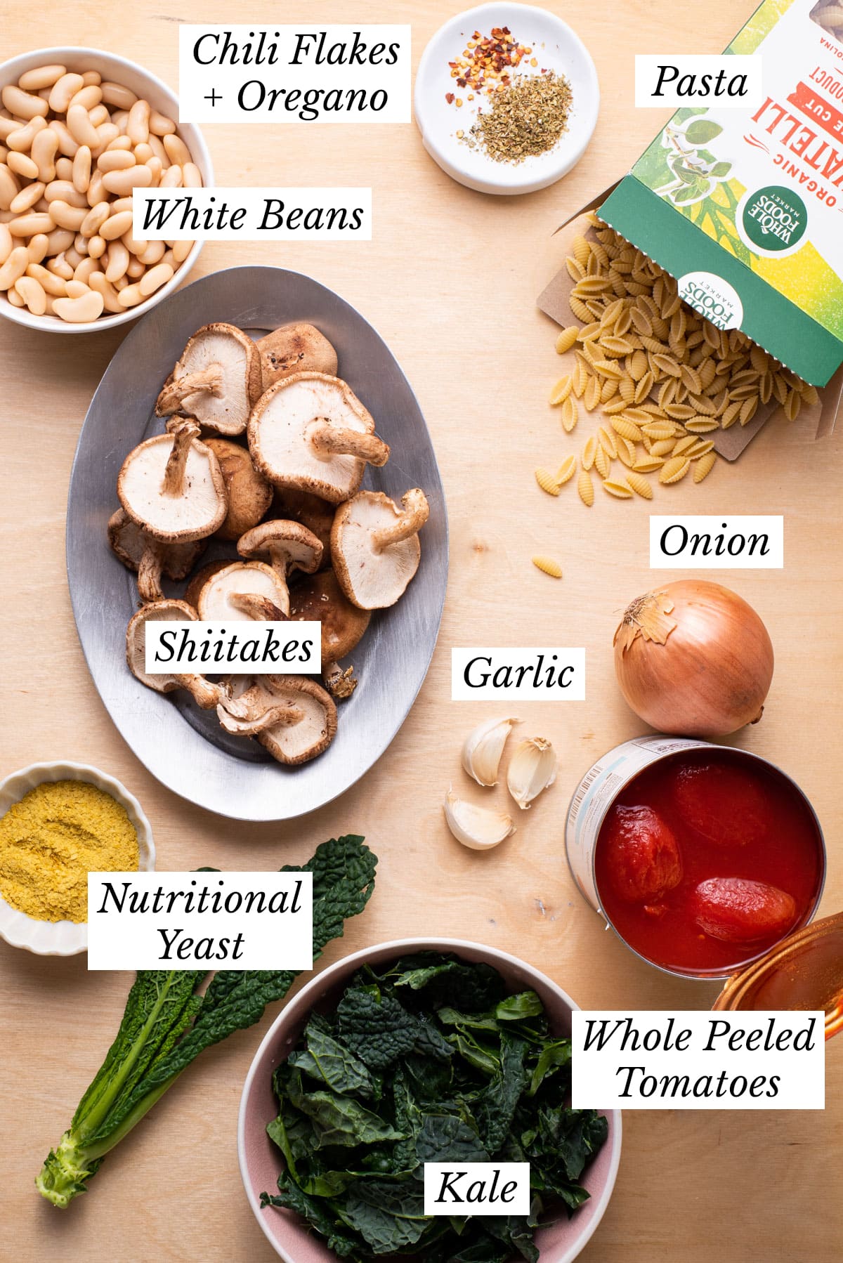 Ingredients gathered on a wooden counter to make vegan pasta with beans.