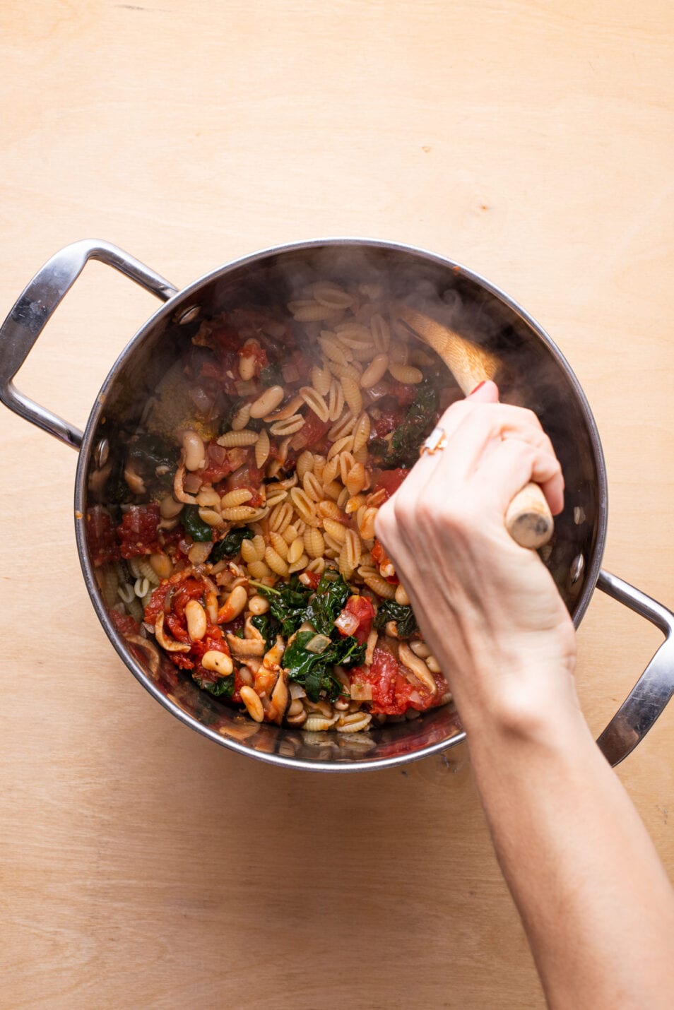 Stirring pasta with beans in a pot.