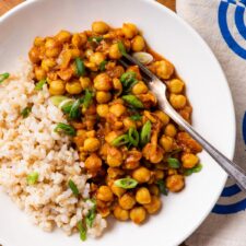 Chana masala in a white bowl with brown rice and scallions.