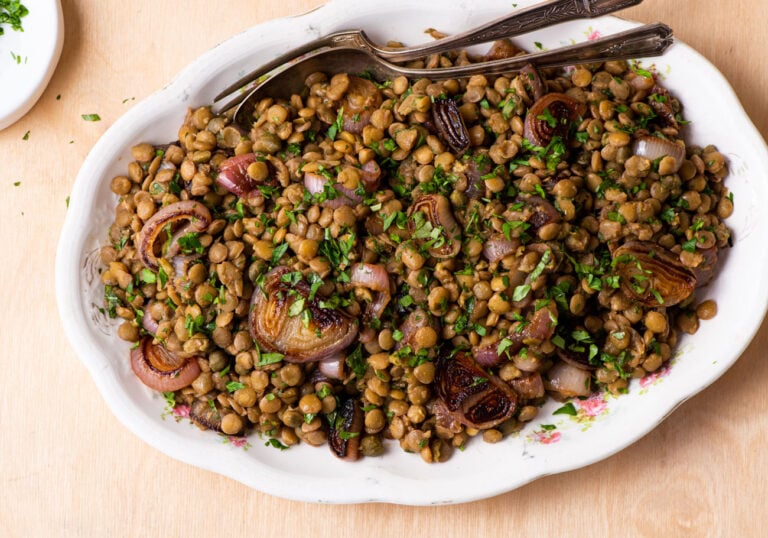 Warm lentil salad with balsamic shallots on a vintage oval platter on a wooden table.