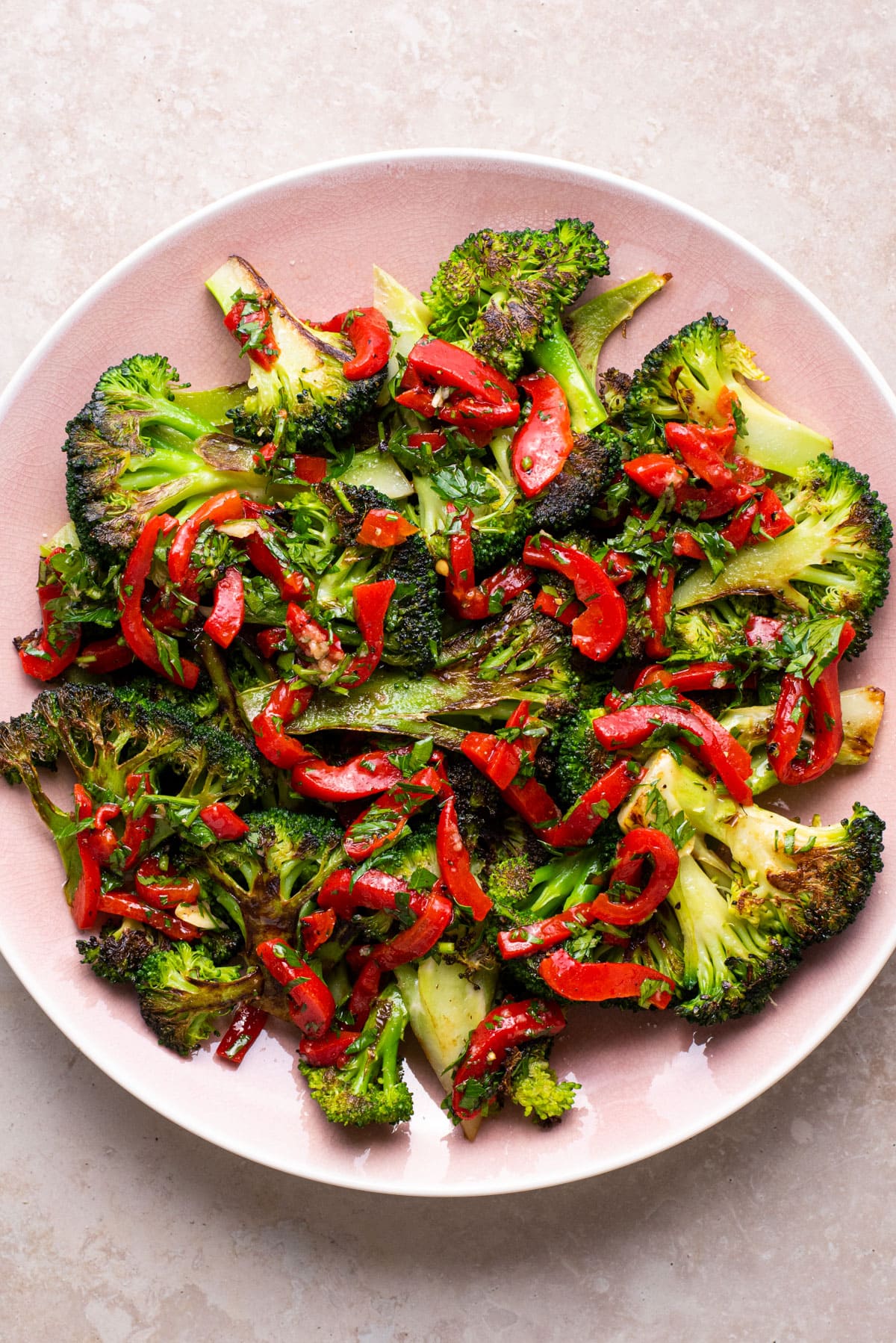 Charred broccoli with red pepper relish on a pink platter.
