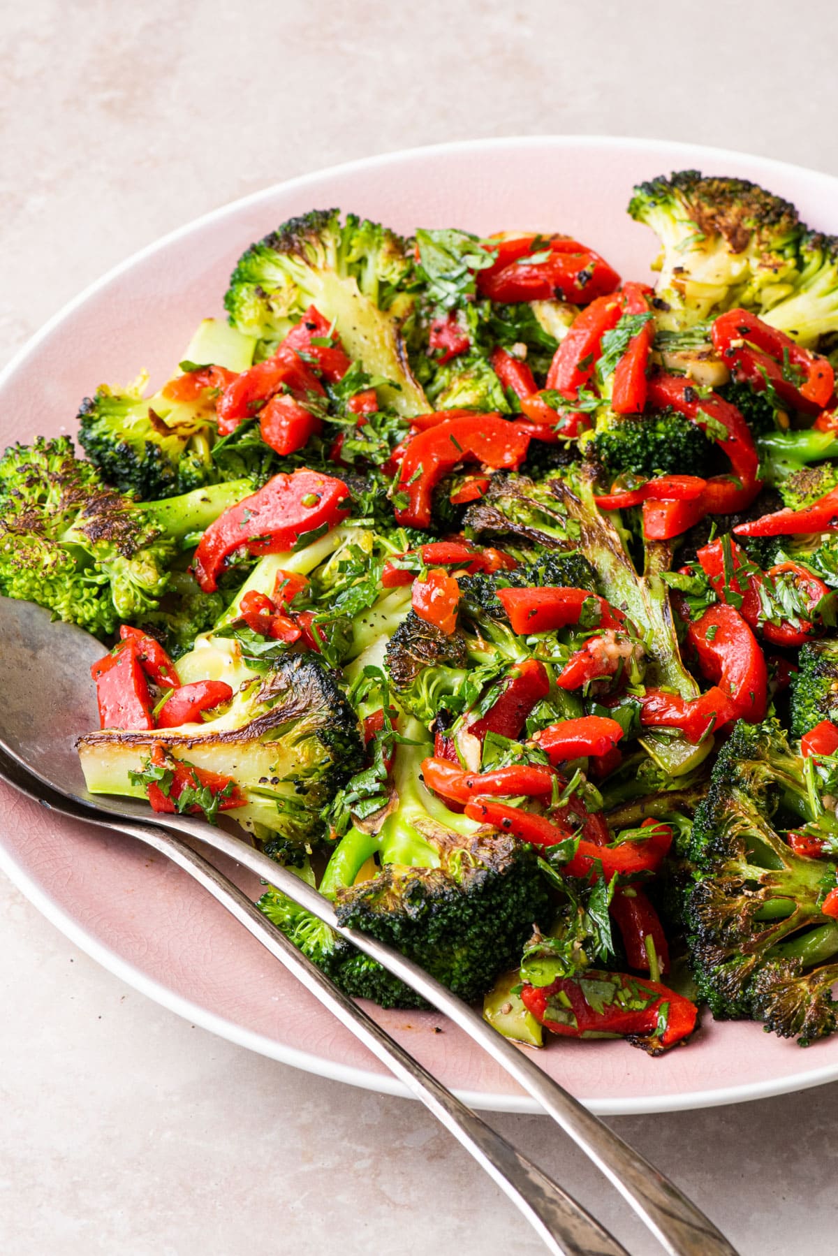 Charred broccoli with red pepper relish on a pink platter.