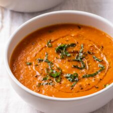 Creamy vegan tomato soup in bowls, garnished with basil and olive oil.