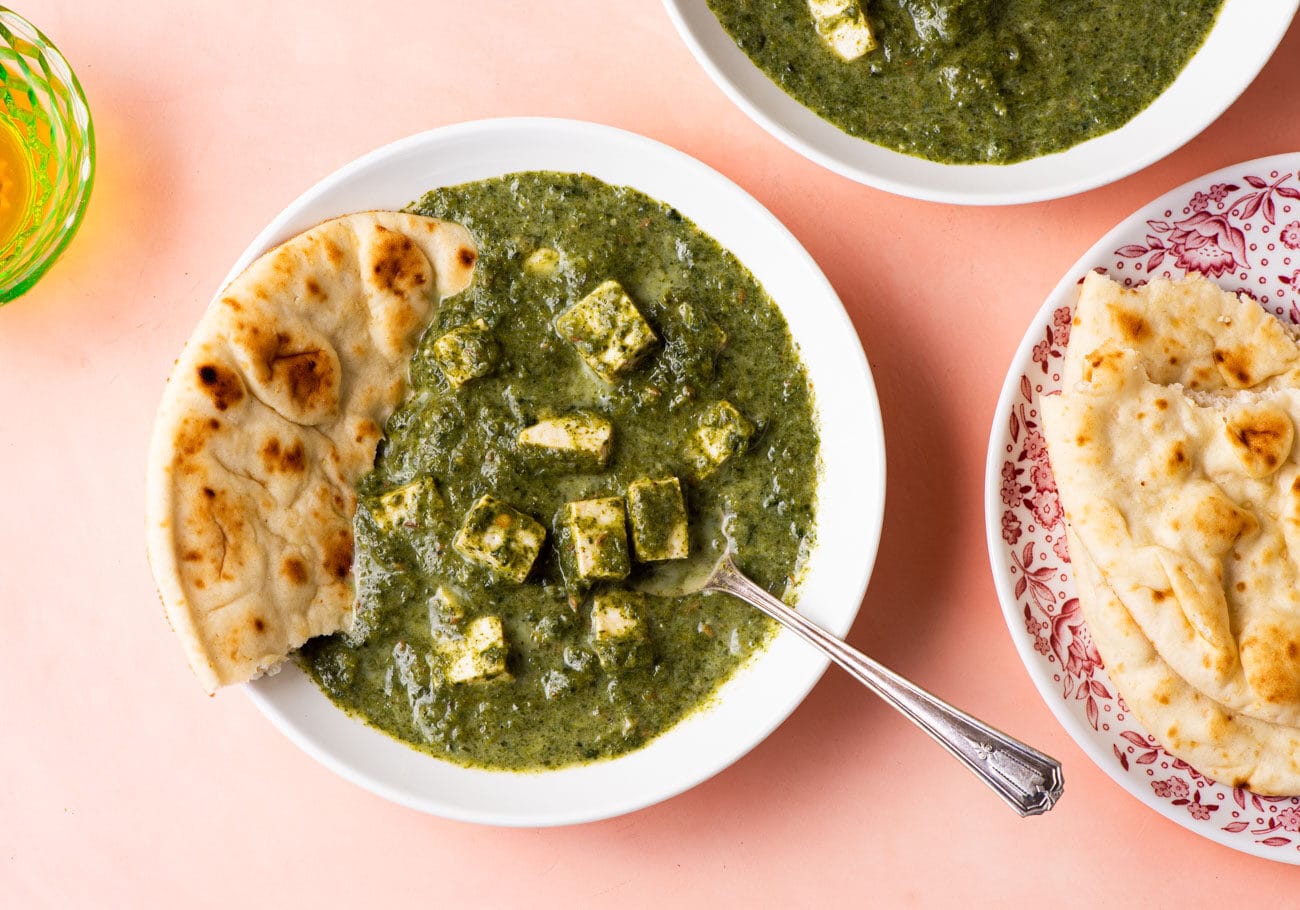 Palak tofu in a white bowl with naan on a pink background.