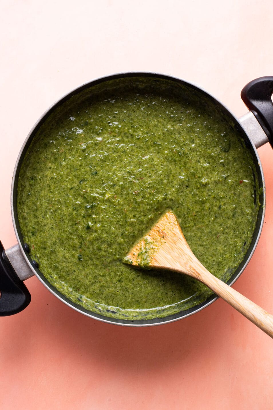 Creamy saag/palak sauce in a pan with a wooden spatula.