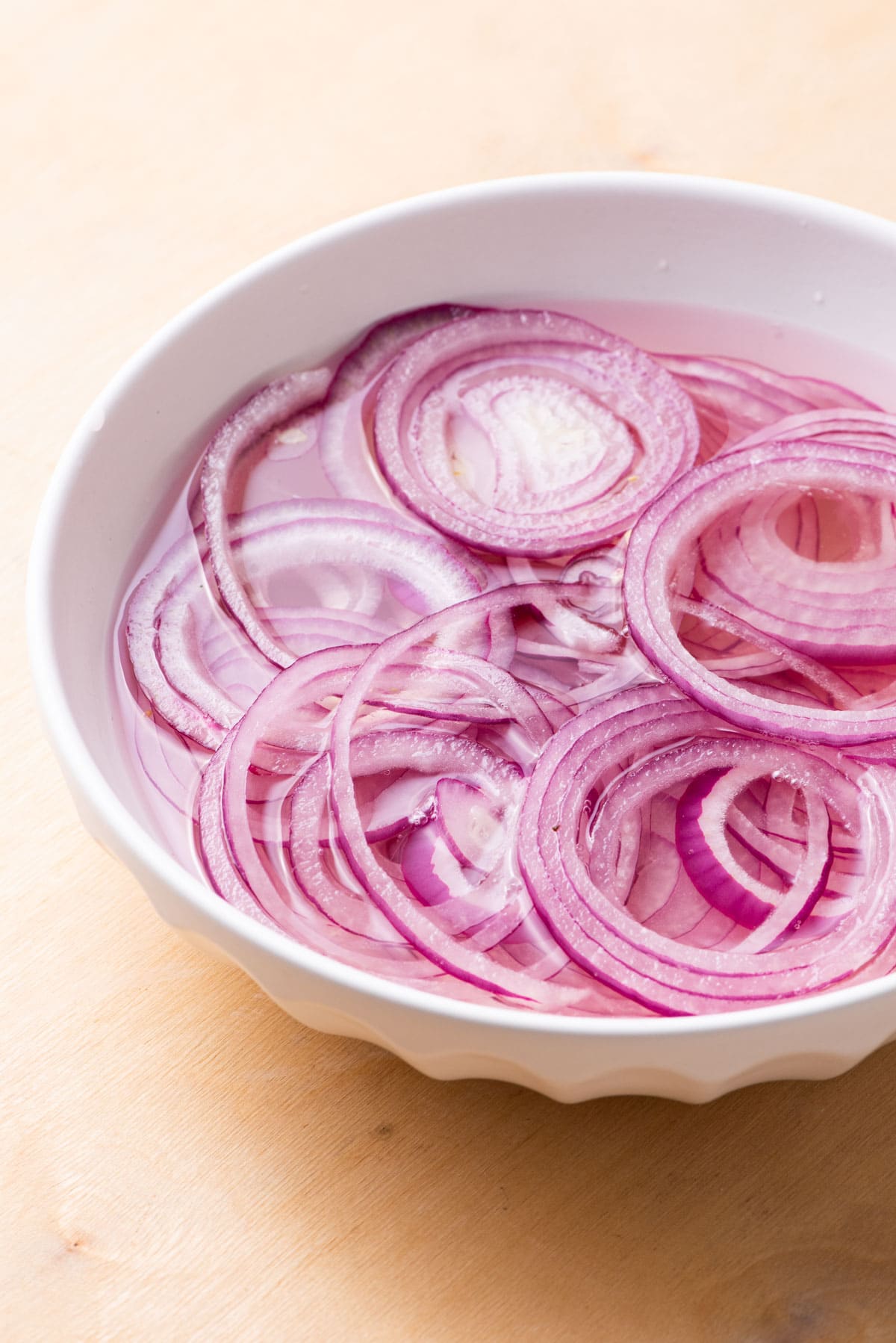 Thin rings of red onion marinating in a bowl of pickling liquid.