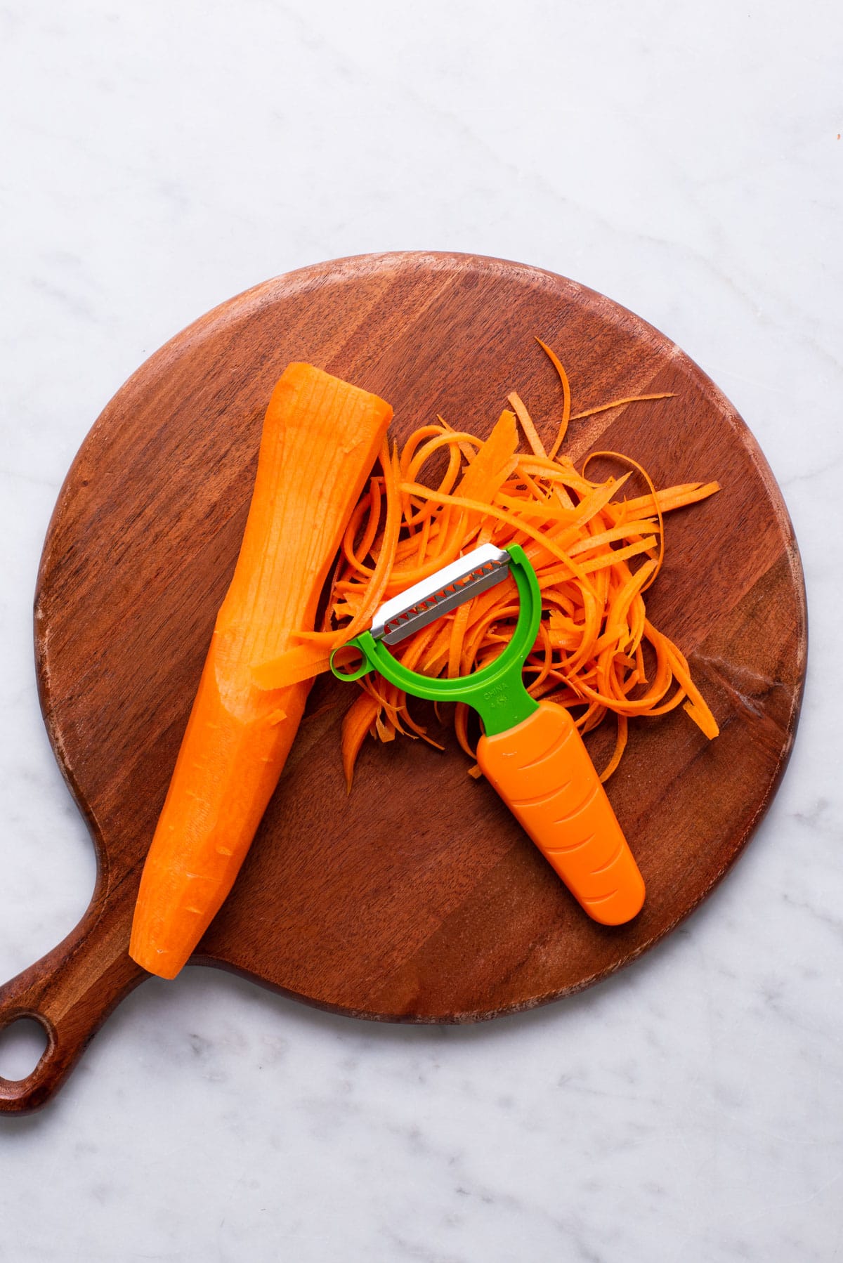 Julienned carrots on a wooden cutting board with a Y-peeler.