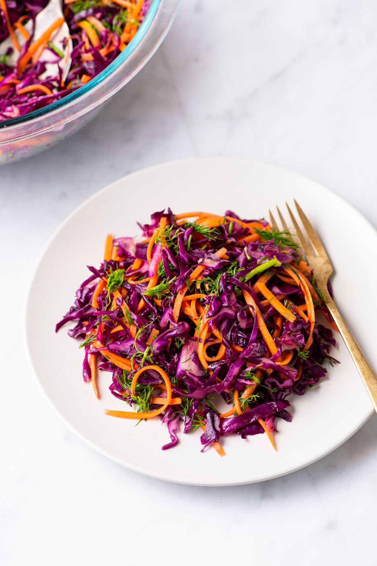 Mayo-less purple cabbage slaw on a beige plate on a marble table.